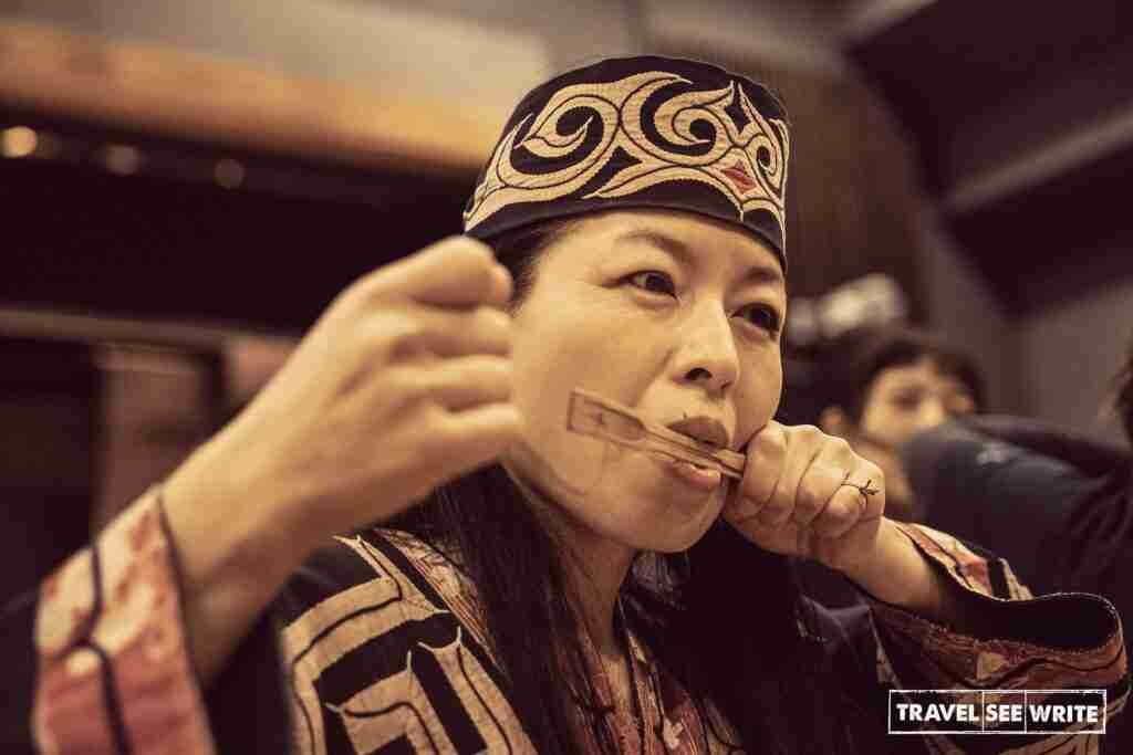 An Ainu artist playing 'Mukkuri' is a traditional mouth harp made of wood (usually bamboo) and a string.