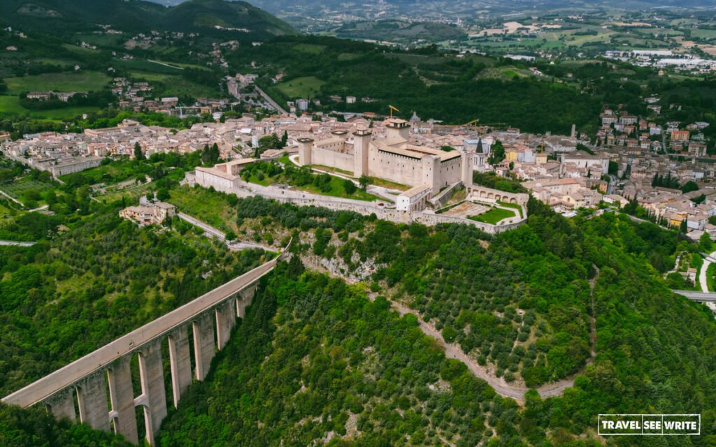 The Rocca Albornoziana fortress overlooks Spoleto while connecting directly to the Ponte delle Torri, a massive 14th-century aqueduct and bridge that spans a deep gorge to link the hill with Monteluco.